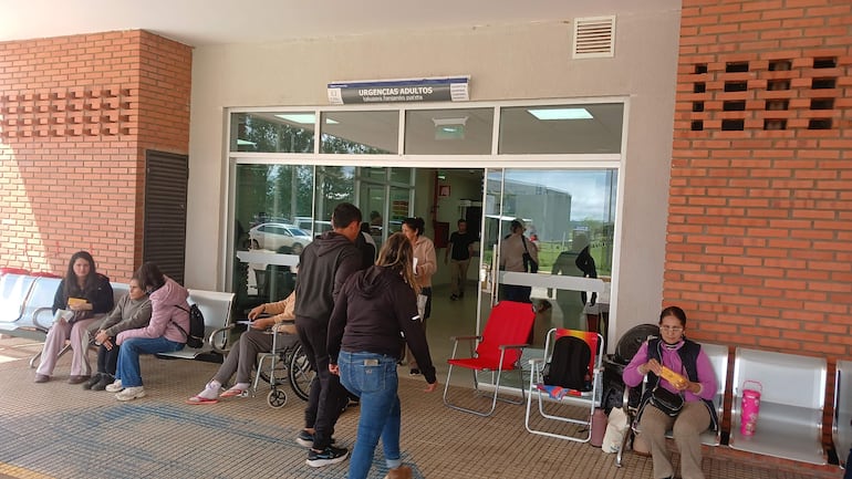 Mujeres sentadas en el área de urgencias del hospital, con expresiones serias. Se observa el letrero 'URGENTES ADULTOS'.