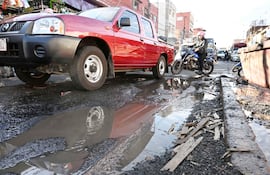 Motociclista parado sobre su moto con casco en una calle con pavimento deteriorado y escombros.
