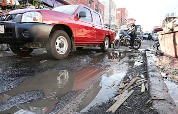 Motociclista parado sobre su moto con casco en una calle con pavimento deteriorado y escombros.