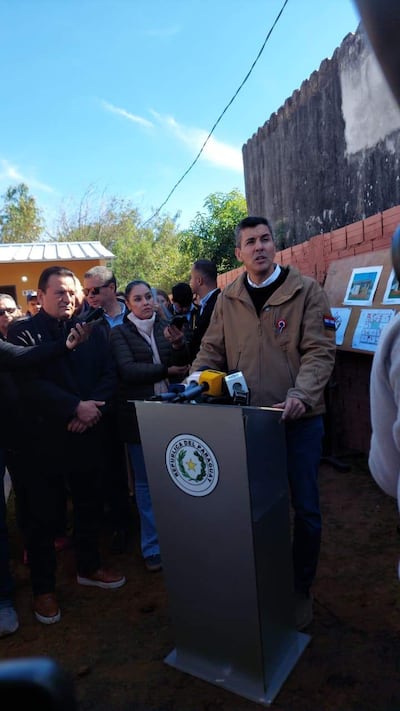 Santiago Peña en chaqueta marrón, detrás de podio, hablando a la multitud que lo escucha atenta.