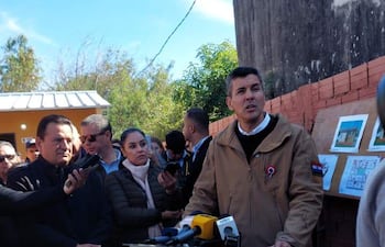 Santiago Peña en chaqueta marrón, detrás de podio, hablando a la multitud que lo escucha atenta.