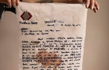 Una mano sostiene un documento desgastado y manuscrito del Ministerio Público relativo a Aldo Alexis Duarte Moreira.