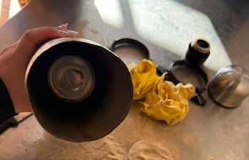 Mano sostiene un objeto cilíndrico en una superficie de cocina con polvo y utensilios dispersos.