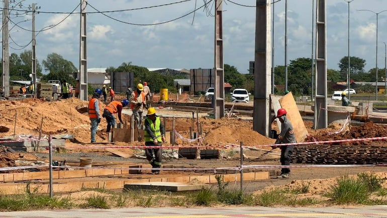 Grupo de trabajadores con cascos y chalecos reflejantes, manipulando materiales en una obra de construcción al aire libre.