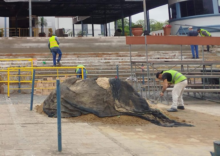 Hombres con chalecos amarillos trabajan en la Basílica de Caacupé, uno limpia gradas, mientras otros usan ladrillos y excavan.