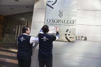 Dos hombres con chalecos de la Superintendencia de Salud colocan un cartel de clausura en el Oropallo Institute en un entorno urbano.