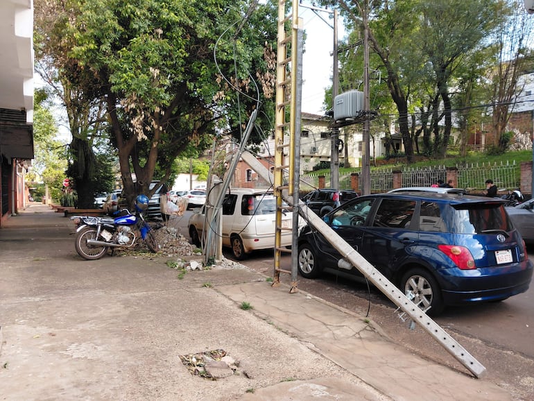 Poste de hierro caído en la calle rodeado de un coche blanco, un coche azul y una motocicleta azul.