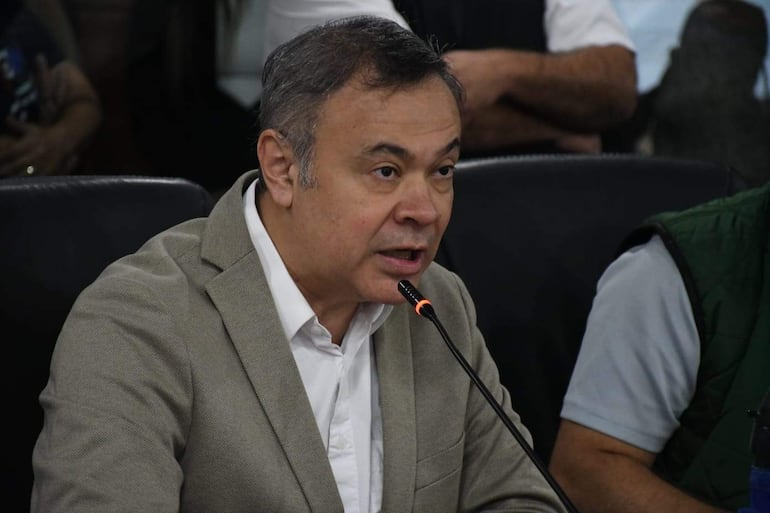 Humberto Blasco en saco beige y camisa blanca, mientras habla con micrófono, en un entorno con público al fondo.