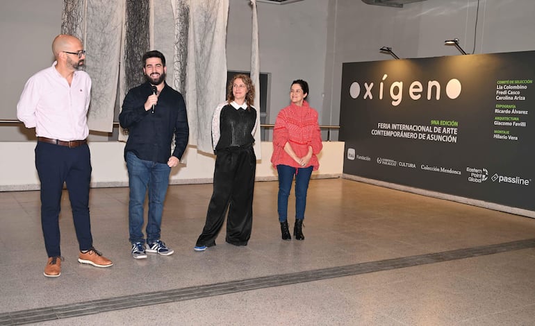 Adriana Ortiz Semidei y tres personas más escuchan atentamente durante un evento cultural, con entorno artísticamente decorado.