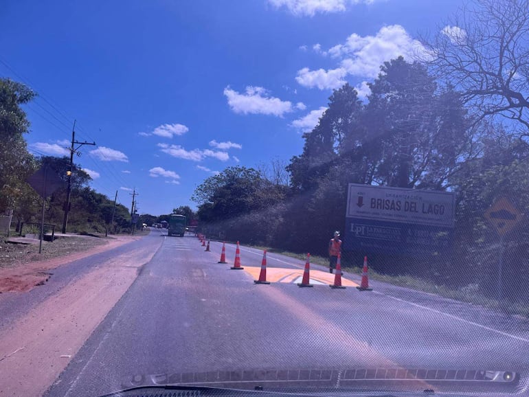 Cartel de 'Brisas del Lago' y conos de tráfico en carretera, con cielo despejado y nubes al fondo.