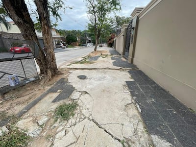 Acera dañada con grietas, árbol a un lado y vehículos estacionados en una calle urbana de Santo Domingo.