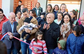 Tres personas al frente cortan cinta en la inauguración, rodeadas de un grupo sonriente en un ambiente festivo.