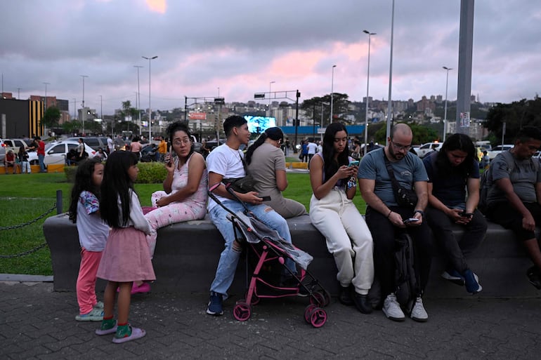Varias personas aguardan en un espacio público con sus teléfonos, en una calle de Caracas. 