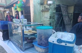 Mujer sostiene globos de colores mientras hombres observan mesa con repostería y alimentos en un ambiente festivo.