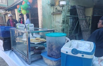 Mujer sostiene globos de colores mientras hombres observan mesa con repostería y alimentos en un ambiente festivo.