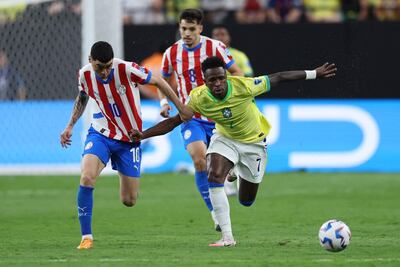 Miguel Almiron intenta contener la carrera de la estrella de Brasil, Vinicius Junior, Damián Bobadilla atento a la acción.