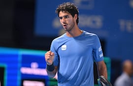 Jugador de tenis con camiseta azul y cabello rizado, levantando el puño en señal de triunfo en un ambiente de torneo.
