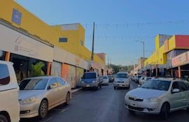 Calle comercial con tiendas coloridas y vehículos estacionados, mostrando un ambiente urbano y activo en Encarnación.