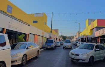 Calle comercial con tiendas coloridas y vehículos estacionados, mostrando un ambiente urbano y activo en Encarnación.