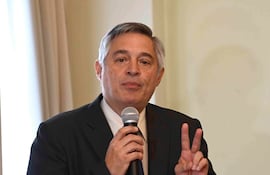 Luis Ramírez, con cabello canoso y traje oscuro, sostiene un micrófono y gesticula con paz en un ambiente formal.