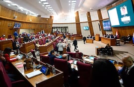 Grupo de diputados en el recinto, algunos de pie y otros sentados, prestando atención al orador en un ambiente moderno.