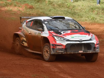 Automóvil de rally Toyota salpicando tierra en un camino, con espectadores observando en el fondo.