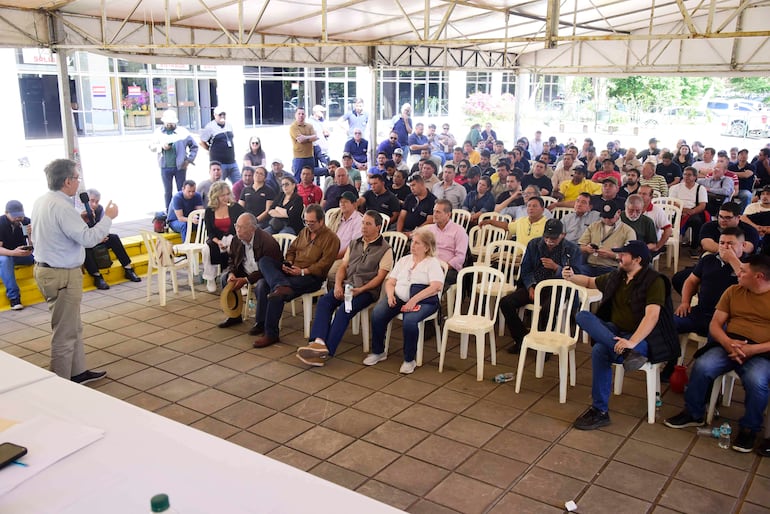 Asistentes al plenario de la ANDE, con predominancia de camisetas de colores, escuchando atentamente al orador de pie con camisa clara.