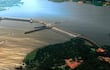 Vista aérea de la represa en construcción sobre el río Paraná, con estructuras hidráulicas y vegetación circundante.