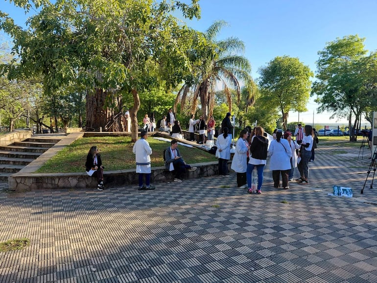 Grupo de bioquímicos en parque, algunos con batas blancas, interactuando en un entorno tranquilo bajo un gran árbol.
