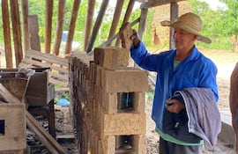 Juan Genaro Fernández, con camisa azul y sombrero de paja, trabaja en un taller de ladrillos al aire libre entre herramientas y ladrillos.