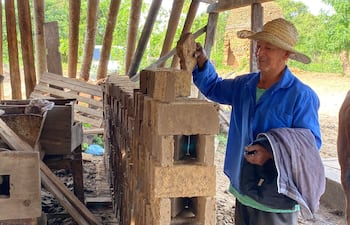 Juan Genaro Fernández, con camisa azul y sombrero de paja, trabaja en un taller de ladrillos al aire libre entre herramientas y ladrillos.