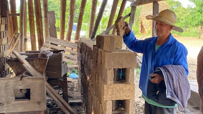Juan Genaro Fernández, con camisa azul y sombrero de paja, trabaja en un taller de ladrillos al aire libre entre herramientas y ladrillos.