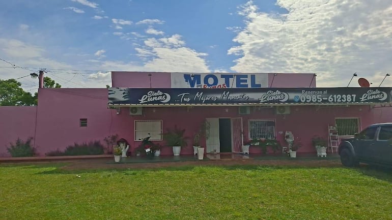Fachada del motel 'Siete Lunas' en color rosa con césped cuidado y letrero visible, sin personas en la escena.