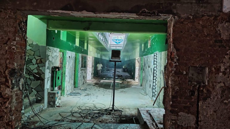 Dos trabajadores con camisetas blancas en un espacio en remodelación, rodeados de polvo y cables eléctricos en el suelo.