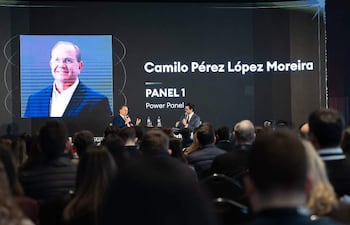 Camilo Pérez López Moreira en traje y micrófono, discutiendo en un panel con un fondo de audiencia formal.