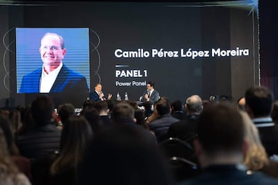 Camilo Pérez López Moreira en traje y micrófono, discutiendo en un panel con un fondo de audiencia formal.