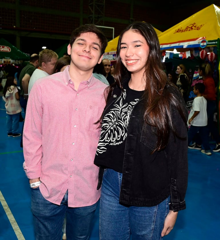 Jóvenes sonrientes, uno con camisa a rayas rosadas y otro con camiseta negra, en un salón decorado.