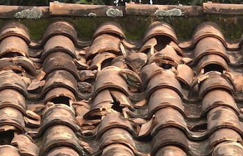 Techo de la escuela con tejas rotas y desplomadas, fragmentos esparcidos y musgo visible en áreas sombreadas.
