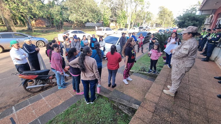 Grupo de personas, mayormente mujeres y niños, escuchan a una mujer en uniforme militar que habla en una manifestación.