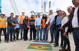 Santiago Peña y Claudia Centurión rodeados de trabajadores con cascos y chalecos reflectantes, celebrando sobre diseño de banderas en el suelo.