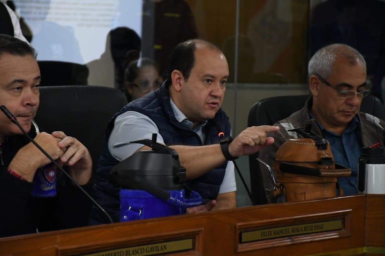 Felix Ayala en camisa clara y chaleco azul habla con gestos, mientras Humberto Blasco escucha atento en el salón de reuniones.