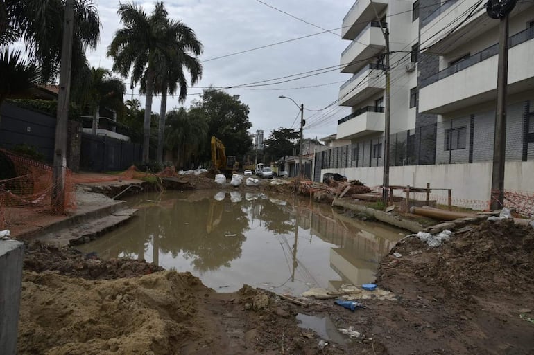 Zona de obras con maquinaria pesada trabajando en un ambiente urbano, rodeada de edificios y malla de seguridad.