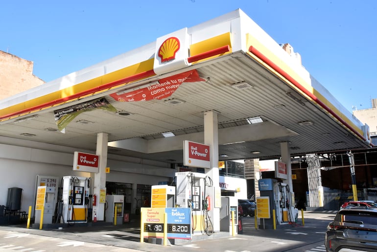 Estación de servicio Shell visible con bombas de combustible y carteles promocionales en un entorno urbano bien iluminado.