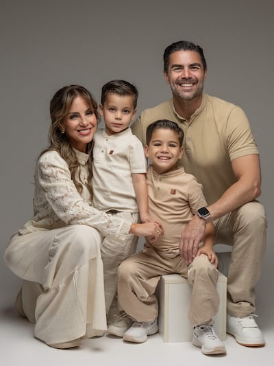 Mujer con blusa clara y falda larga, dos niños en camisetas claras y un hombre con camiseta clara, todos sonriendo juntos.