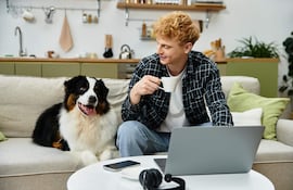 Hombre joven de cabello rizado y rubio sentado con una taza blanca, junto a un perro feliz en un ambiente moderno.