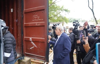 Isaías Fretes, canoso y con abrigo oscuro, revisa un contenedor metálico rojo mientras periodistas observan con atención.