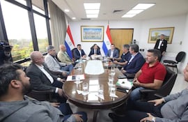 Hugo Joel Meza y Raúl Luis Latorre Martínez sentados en mesa ovalada en ambiente formal, rodeados de documentos y dispositivos móviles.