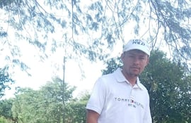 Hombre joven de pie en ambiente rural, lleva camiseta blanca de Tommy Hilfiger y jeans, con expresión tranquila y gesto de pulgar arriba.