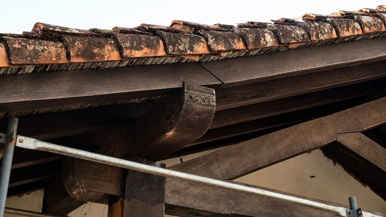 Techumbre de casa colonial con tejas terracota, madera expuesta y musgo, en un entorno rural.