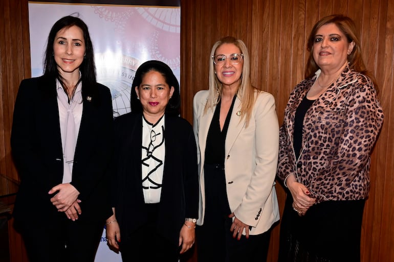 Cuatro mujeres de pie, una con traje negro, otra con gafas, una en blazer claro y una en vestido de leopardo, sentidas en conversación.